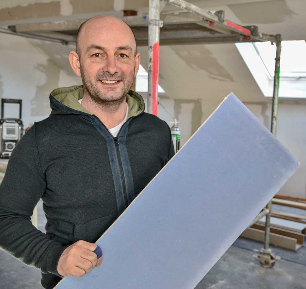 Ein Mitarbeiter vom Henrich Baustoffzentrum hält ein Bauplatte in der Hand